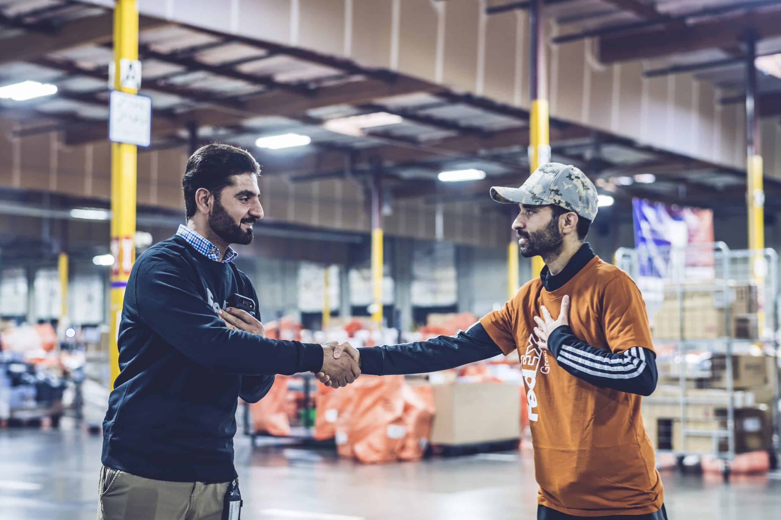 World Relief, Seattle, WA, October 20, 2022. Ahmad Samim (orange shirt) and Mudeer Rohilli interact with Steven Body at at Fedex sorting and distribution facility in Kent, WA. Sean Sheridan Photographs.