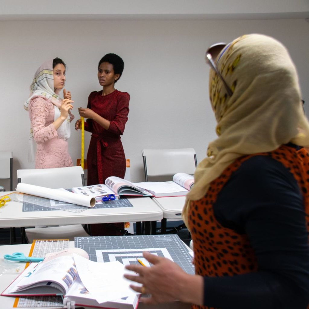 Refugee women measure each other for sewing class.