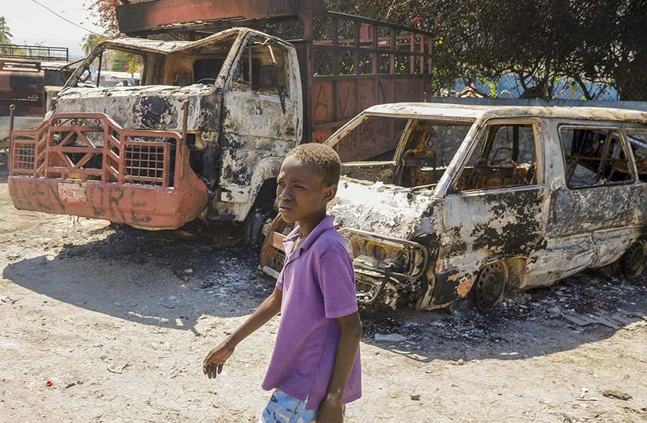 Current humanitarian crisis: A youth walks by charred cars outside a police station in Port-au-Prince, Haiti. Photo Credit: AP Photo/Odelyn Joseph