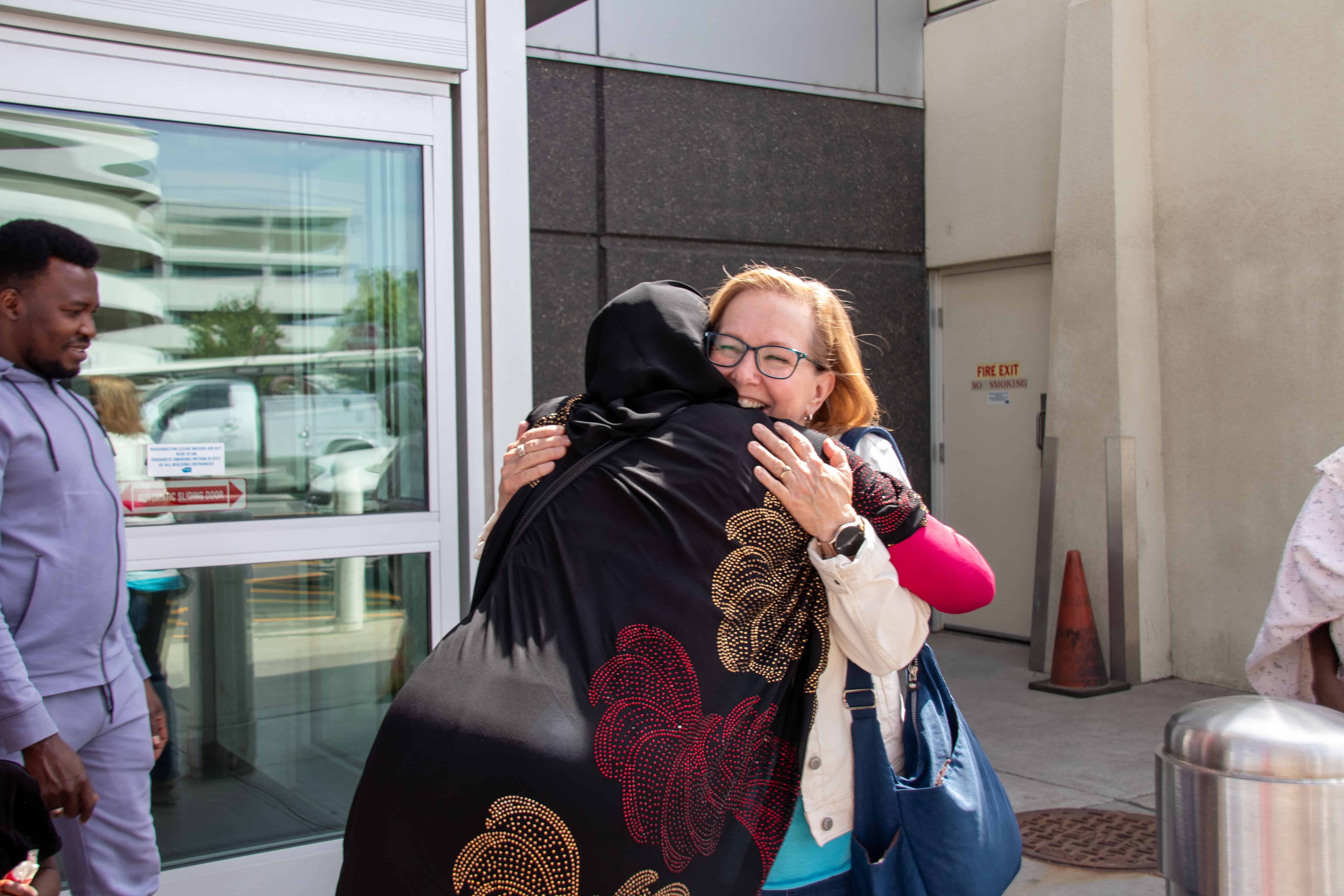 Two women welcome each other with smiles on their faces.