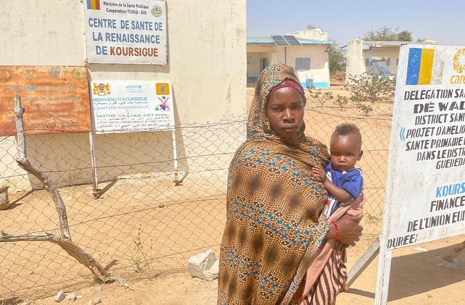 Nadiwa's refugee story - Nadiwa stands in front of a health facility holding one of her children