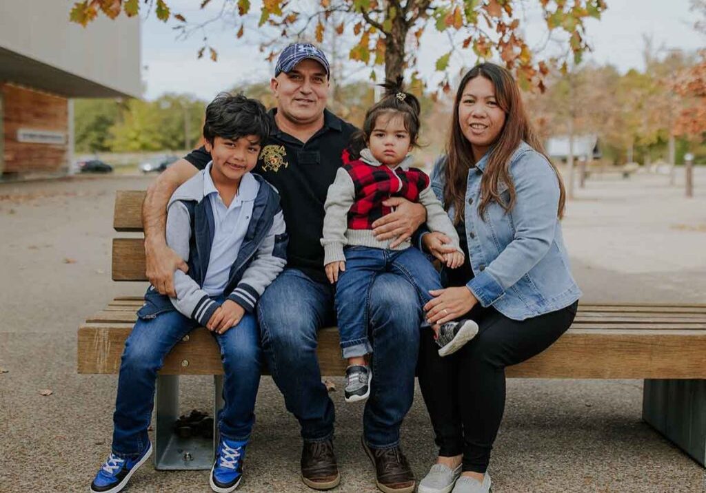 Imagrant fimily sitting on bench outside smiling at camera