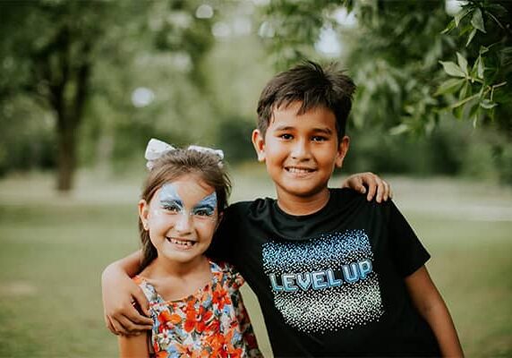 A boy puts his arm around a young girl who is wearing facepaint as they look at the camera