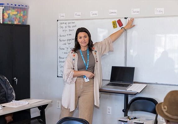 A woman is pointing to a whiteboard teaching a class
