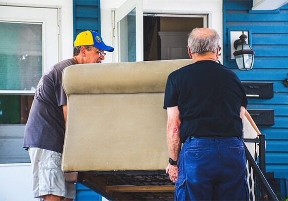 Two men move a couch into a home
