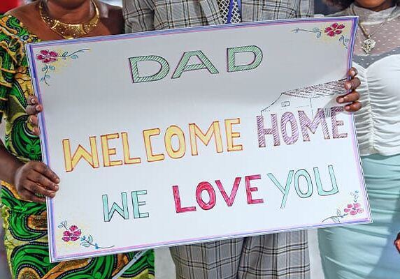 A family holds a sign that reads "Dad Welcome Home We Love You"